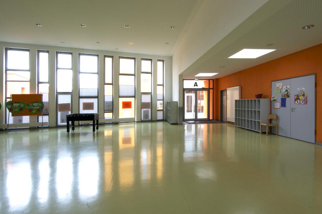 Das Forum bildet das Zentrum der neuen Schule und ist sowohl Aula als auch Sportstätte. Innenraum mit Blick zu einer bodentiefen Fensterfront und Eingang mit Windfang.